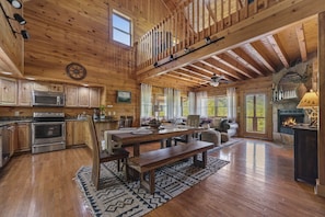 A spacious wooden cabin with a large dining table, kitchen with modern appliances, and a cozy fireplace.