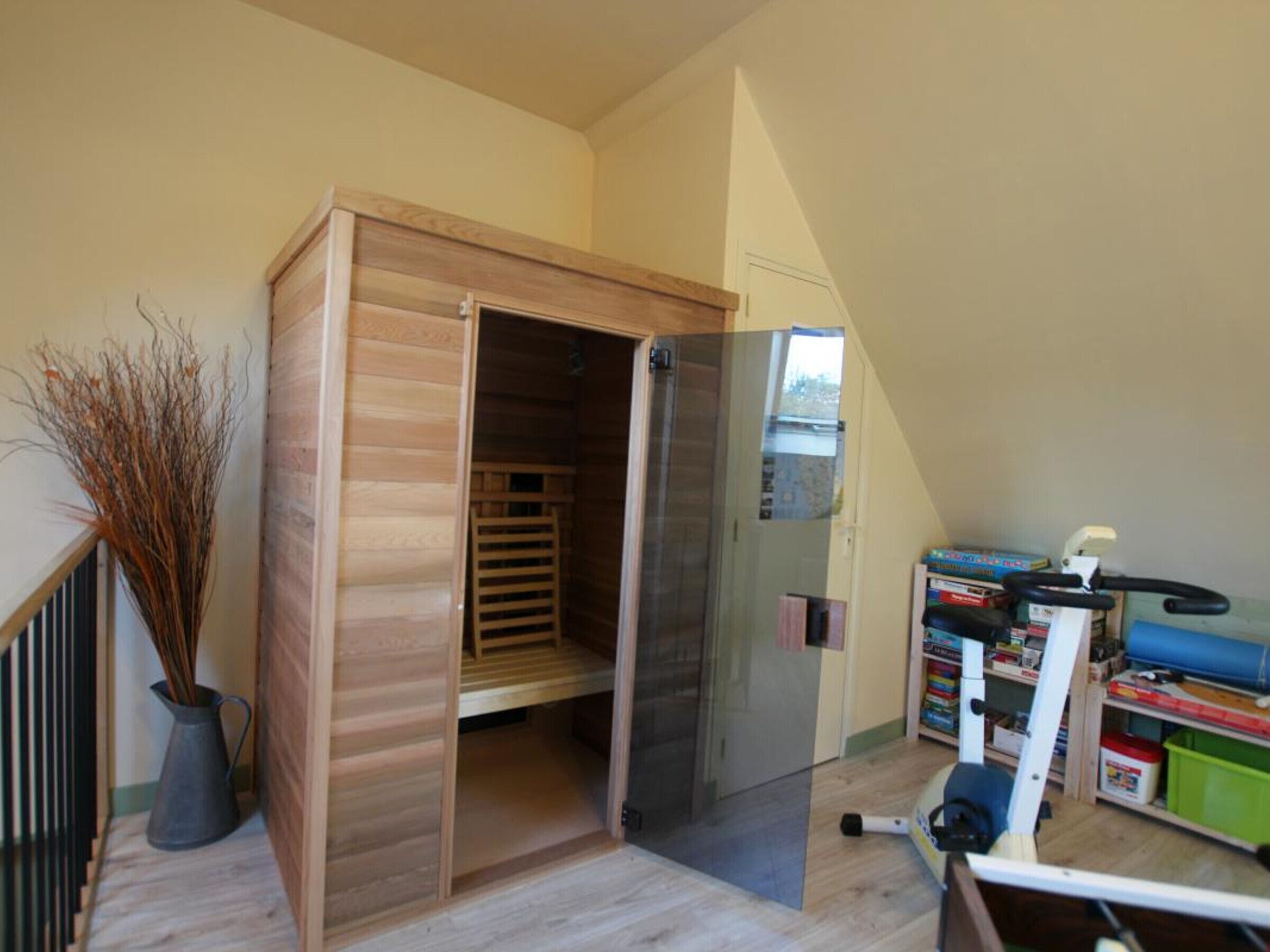 A room with a wooden wardrobe, a bookshelf, and a vacuum cleaner.