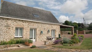 A stone building with a sloped roof, a small porch, and a garden with various plants. - Stone house near the sea with sauna and large garden (Baubigny)