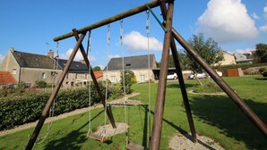 A wooden swing set in a grassy area with houses in the background. - Stone house near the sea with sauna and large garden (Baubigny)