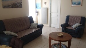 A living room with a sofa, two armchairs, a coffee table, and a door leading to a balcony. - Stone house near the sea with sauna and large garden (Baubigny)