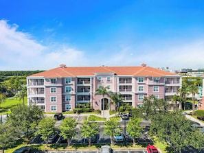 A multi-story hotel with a red-tiled roof, balconies, and a parking lot with trees.