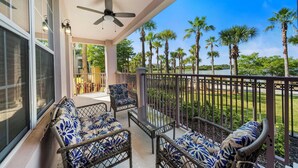 A balcony with wicker furniture, a ceiling fan, and a view of palm trees. - Lakeview - Next to Clubhouse, Gym and Pool - 1st Floor (Orlando)