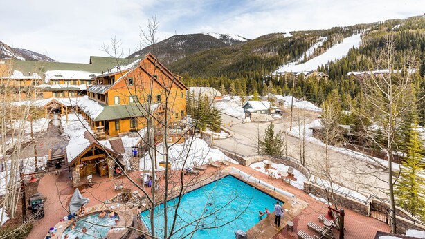 A resort with a swimming pool, outdoor seating, and a mountainous backdrop.