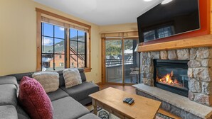 A living room with a stone fireplace, a gray sofa, and a large window overlooking a mountain.