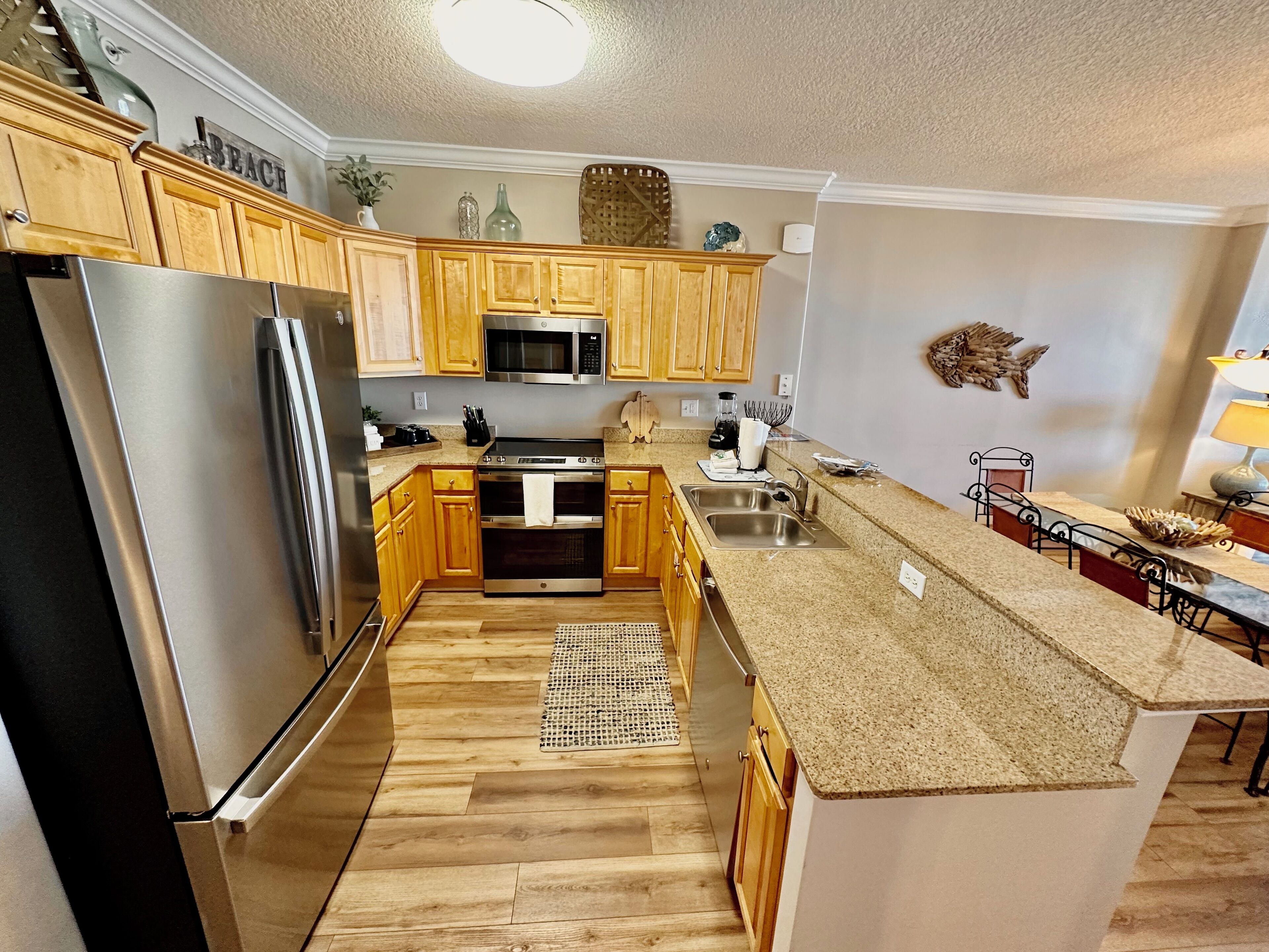 A modern kitchen with wooden cabinets, stainless steel appliances, granite countertops, and a small island with a sink.