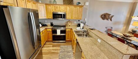 A modern kitchen with wooden cabinets, stainless steel appliances, granite countertops, and a small island with a sink.