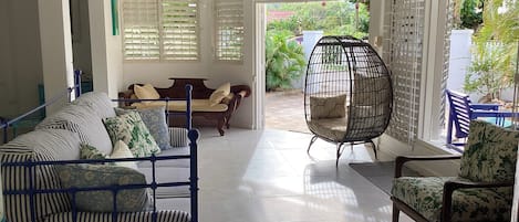 A spacious room with a blue metal-framed sofa, a hanging egg chair, and a wooden sofa with patterned cushions.