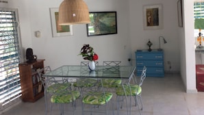 A dining area with a glass table and metal chairs, a vase with flowers, a blue cabinet, and a painting on the wall.
