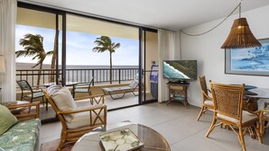 Un balcon avec vue sur l’océan, aménagé avec des fauteuils et une table en osier, et un téléviseur fixé au mur.