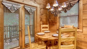 A wooden interior with a round dining table, chairs, and a chandelier.