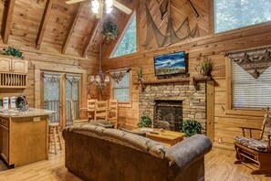 A cozy cabin interior with a stone fireplace, wooden furniture, and a large window overlooking the forest.