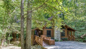 A cabin with a porch and a stone wall, surrounded by trees.