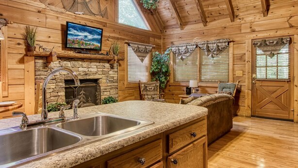A cozy cabin-style kitchen with a stone fireplace, granite countertops, and wooden cabinetry.