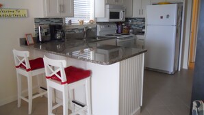 A kitchen with white cabinets, a central island with bar stools, a microwave, stove, and refrigerator. - Reduced  rates  on 30A beach front condo. (Santa Rosa Beach)