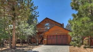 A wooden cabin with a garage, surrounded by trees. - Villa Grove Lodge by Destination Big Bear : Garage Parking! Pool Table! Outdoor Hot Tub! WiFi! Gas BBQ! (Big Bear City)