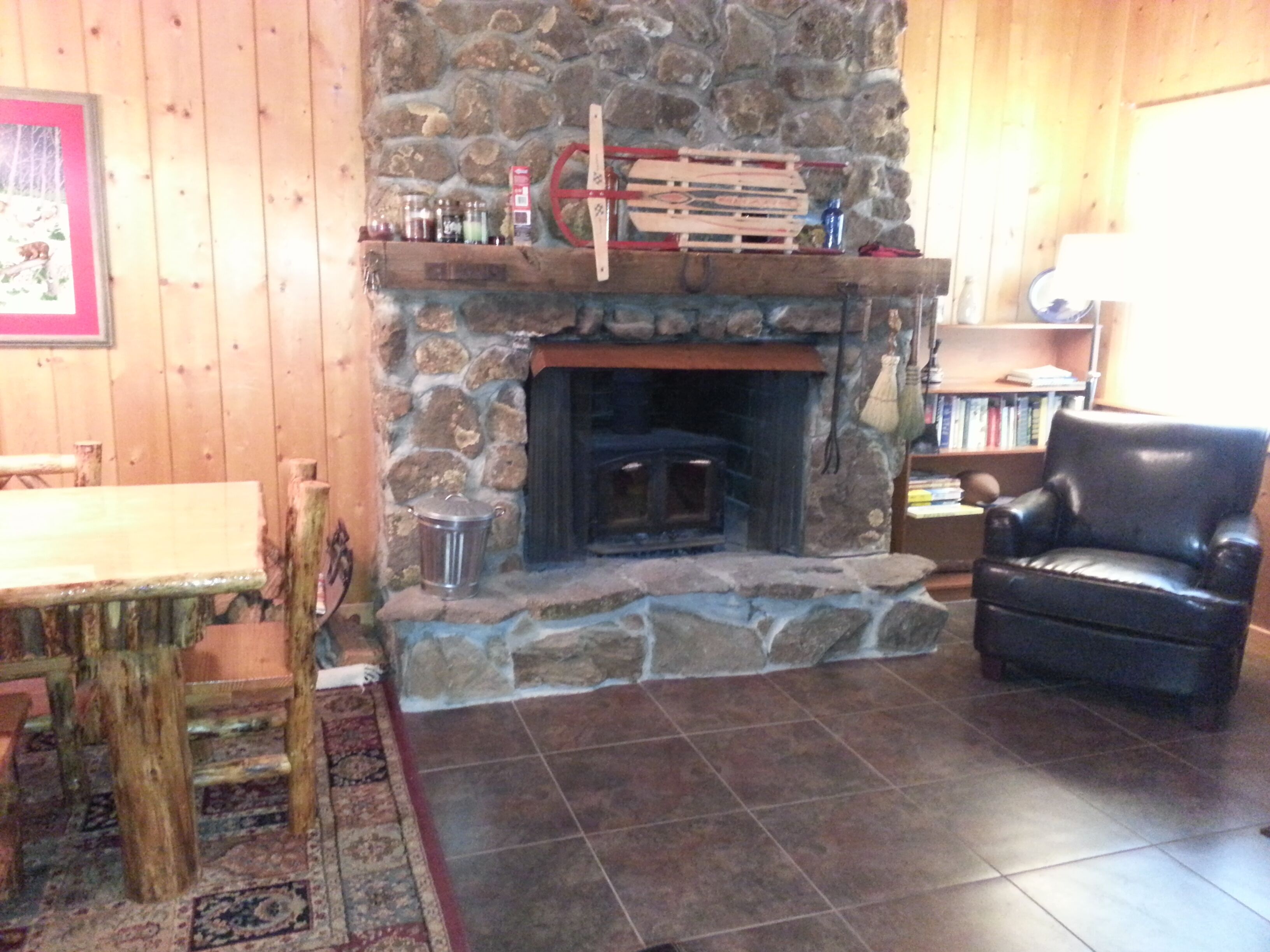 A cozy room with a stone fireplace, a wooden table, a leather chair, and a bookshelf.