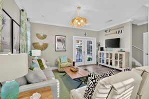 A living room with a sofa, armchair, and a coffee table. There is a television on a cabinet and a door leading outside.