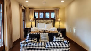 A bedroom with a bed, two bedside lamps, a checkered sofa, and a window with curtains.