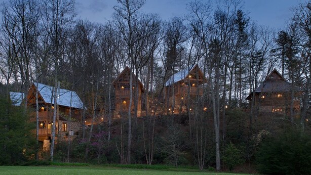 A cluster of log cabins with multiple levels and balconies, surrounded by a forested area.