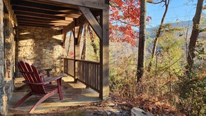 A wooden porch with a stone wall, a red Adirondack chair, and a view of autumn foliage.