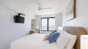 A hotel room with a bed, a ceiling fan, a TV, a window with a view, a bedside table with a lamp, and a painting on the wall. - 2 BR @ Island Winds West - *Beach Front* (Gulf Shores)