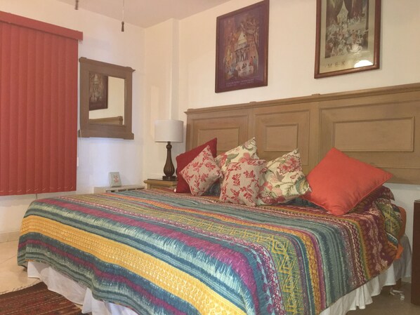 A bedroom with a large bed, a wooden headboard, a nightstand with a lamp, and a framed picture on the wall.