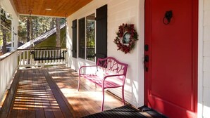 A covered porch with a red door, a bench, and a wreath on the wall.