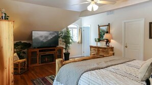 A bedroom with a bed, a television, a wooden cabinet, a mirror, and a ceiling fan.