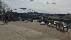 A paved walkway with benches, a cyclist, and a bridge in the background.