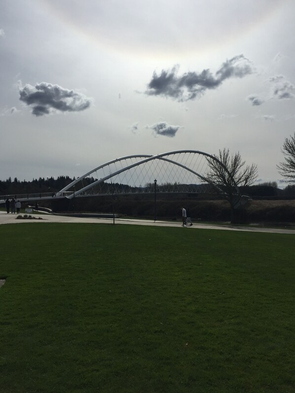 A large, open grassy field with a distinctive arched bridge structure in the background.