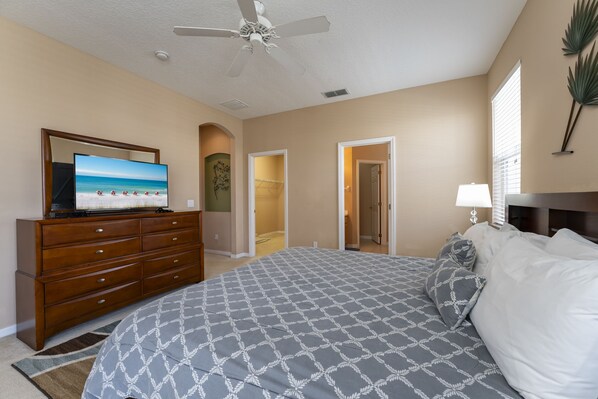 Quarto com cama, cômoda, televisão, ventilador de teto e vista para a praia pela janela.
