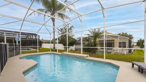 Une piscine entourée d’une clôture blanche et dotée d’une structure en verre, avec des palmiers en arrière-plan.