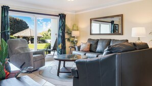 A living room with a grey armchair, a black leather sofa, a glass coffee table, and a small side table with a lamp. - Fun, Easy & Sunset Views! Ground Floor Escape – Islander 114 (Destin)