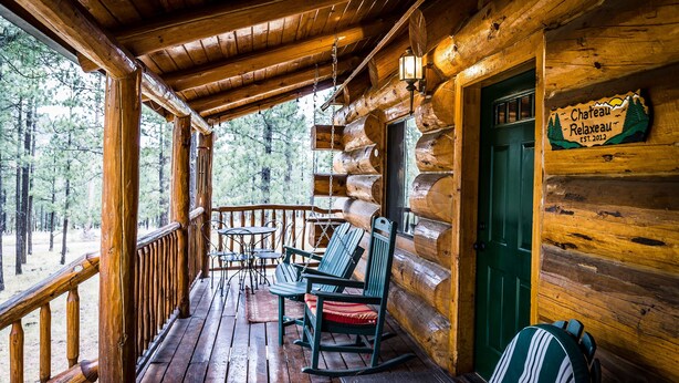Une cabane en rondins de bois avec une véranda, des fauteuils à bascule et une enseigne indiquant : « Château de la détente ».