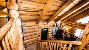 Un escalier en bois à l’intérieur d’une cabane en rondins, avec une porte verte et un canapé en cuir noir.