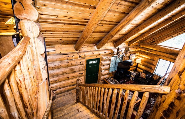 A wooden staircase in a log cabin interior with a green door and a black leather couch.