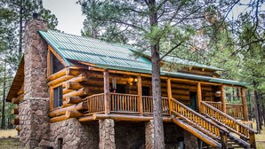 Une cabane en rondins, avec des fondations en pierre, un revêtement extérieur en bois et un toit en métal vert.