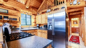 Une cuisine rustique, située dans une cabane en bois, avec un plan de travail en granit, des appareils électroménagers en acier inoxydable et un tapis rouge à motifs.