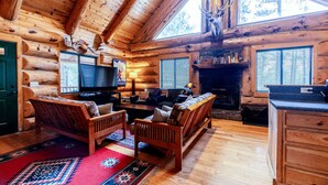 L’intérieur d’une cabane en rondins, avec un plafond en bois, une cheminée, un téléviseur et un coin salon confortable.