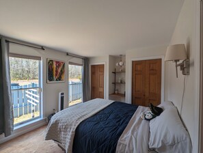 A bedroom with a bed, a window, a door, and a wall-mounted shelf.