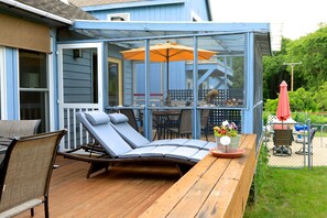 A covered outdoor deck with lounge chairs, a table, and a patio umbrella.