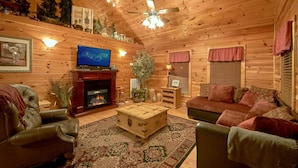 Un intérieur chaleureux de chalet en bois, avec une cheminée, des meubles en cuir, un téléviseur et des objets de décoration.