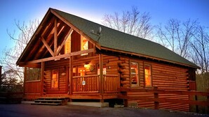 Une cabane en rondins dotée d’une véranda, de grandes fenêtres et d’une cheminée.