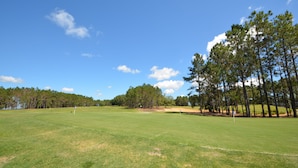 Een golfbaan met een heldere lucht, groen gras en bomen.