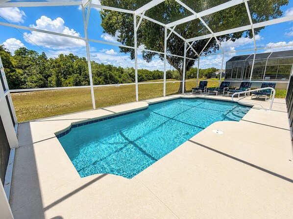 A swimming pool with a covered area, lounge chairs, and a view of the surrounding greenery.