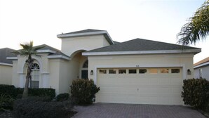 Een gelijkvloers huis met garage, een oprit van baksteen en een palmboom.