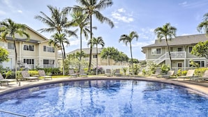 Ein Swimmingpool mit Liegestühlen und Palmen, umgeben von Gebäuden mit Balkonen.