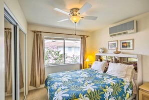 A bedroom with a bed, a ceiling fan, an air conditioner, a window with curtains, and a lamp. - Kapolei Condo w/ Lanai & Pool Access - Near Beach! (Kapolei)