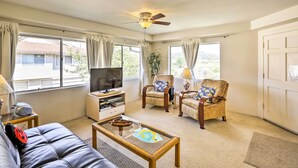 Ein Wohnzimmer mit einer Couch, zwei Sesseln, einem Couchtisch, einem Fernseher und einem Deckenventilator.